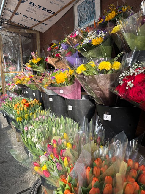 A display of various fresh flower bouquets arranged in black buckets and on a stand, featuring a variety of colorful blooms including yellow chrysanthemums, purple irises, white tulips, red roses, and